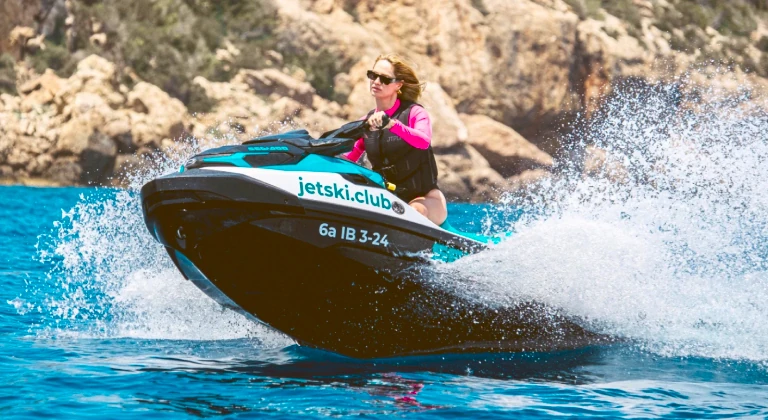 jet-ski-tour-ibiza-action-jetskiclub Woman riding a Sea-Doo jet ski fast during a guided jet ski tour with jetski.club in Ibiza turquoise Mediterranean waters