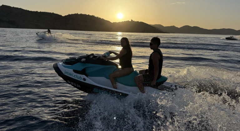 Pareja disfrutando de un tour en moto de agua al atardecer en Ibiza con la isla de Ibiza al fondo